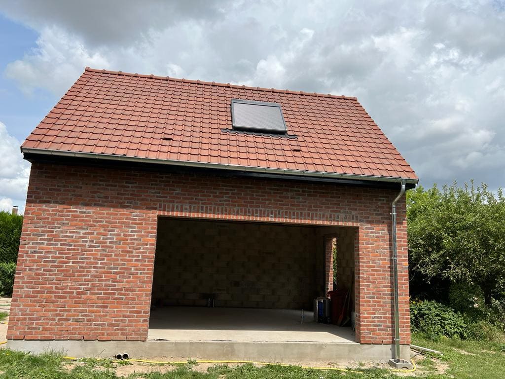 Toiture terminée par Applitech Enveloppe sur une extension de garage à Baisieux. La couverture est réalisée en tuiles mécaniques de terre cuite rouge, incluant une fenêtre de toit (Velux) et une descente d'eau pluviale en zinc parfaitement raccordée à la gouttière.