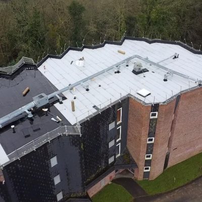 Vue aérienne du site Applitech Enveloppe à Bonsecours : bâtiment industriel à toiture plate, partiellement sombre et partiellement claire, entouré de zones végétalisées et de terrains en travaux.