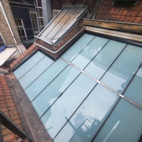 Vue aérienne d'une verrière de toiture entièrement rénovée par Applitech Enveloppe à Lille. Les nouveaux éléments verriers sont clairs et propres, offrant une finition moderne avec des profilés d'étanchéité neufs, intégrés parfaitement entre les toitures en tuiles et les murs en briques.