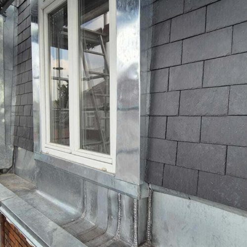 Détail d'une toiture neuve en couverture zinc à joints debout avec habillage en ardoise, réalisée par Applitech Enveloppe, incluant chéneau et fenêtre en encadrement zinc.
