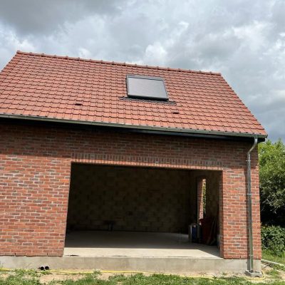 Toiture terminée par Applitech Enveloppe sur une extension de garage à Baisieux. La couverture est réalisée en tuiles mécaniques de terre cuite rouge, incluant une fenêtre de toit (Velux) et une descente d'eau pluviale en zinc parfaitement raccordée à la gouttière.