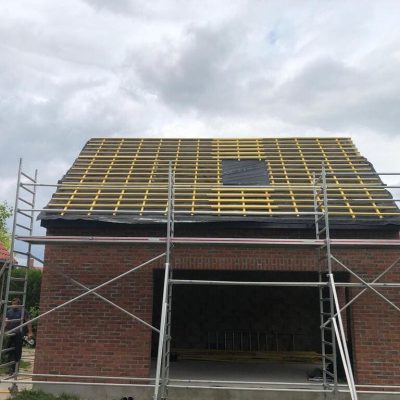 Chantier Applitech Enveloppe à Baisieux montrant l'étape de liteautage sur une extension de maison en briques rouges. La charpente est recouverte d'un écran de sous-toiture noir et de liteaux en bois neufs, prête pour la pose des tuiles. Un échafaudage de sécurité entoure la structure.